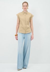 Camicia a maniche corte khaki con colletto, abbinata a jeans a gamba larga di un blu chiaro. Tessuto testurizzato. Design semplice senza motivi.