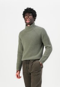 Ribbade olivgröna polo tröja i stickat material, kombinerad med mörk olivfärgade joggarbyxor med elastisk midja och sidofickor.