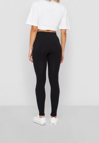 Svarta leggings med en åtsittande design, tillverkade av ett stretchmaterial, med hög midja och slät yta. Bärs med en vit kort topp.