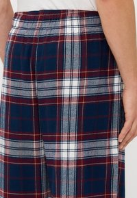 Marine- og burgunderrutete pysjamasbukser med en myk tekstur, med elastisk liv og hvite detaljer i mønsteret.