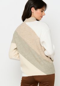 Maglione a maglia con blocchi di colore diagonali in beige, bianco, verde chiaro e crema, dotato di un colletto alto e una texture morbida.
