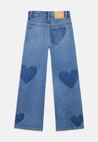 Lyseblå denimwide-leg jeans med to mørkere blå hjerteformasjoner på bena og en rektangulær beige etikett bak på livet.