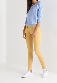 Vaaleansininen pitkähihainen paita ja keltaiset kapeat farkut; valkoiset lenkkarit. Asussa on rento istuvuus ja sileä kangas mukavuutta varten.