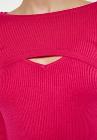 Tæt siddende ribbet top i lys pink med bred udskæring og en diamantformet udsparing i midten, med en diskret tekstur i stoffet.