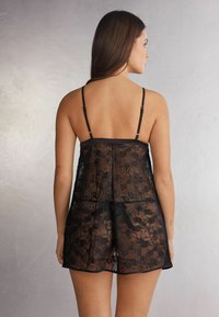 Camisola nera in pizzo con motivo floreale, design traslucido, spalline regolabili e vestibilità ampia, caratterizzata da orlo dritto sopra la metà della coscia.