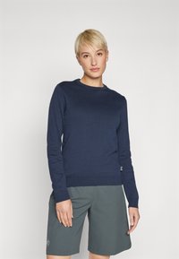 Marinblå stickad tröja med långa ärmar, rund halsringning och ribbad nederkant; matchad med grå shorts med en logotyp på benet.