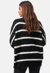 Gestreifter schwarz-weiß gestrickter Pullover mit lockerem Schnitt, langen Ärmeln und einer strukturierten Materialbeschaffenheit. Die Rückseite zeigt horizontale Streifen.