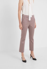 Pantaloni a fantasia in rosso, bianco e blu navy con vestibilità slim, vita media e lunghezza corta, abbinati a tacchi neri e una maglia bianca.