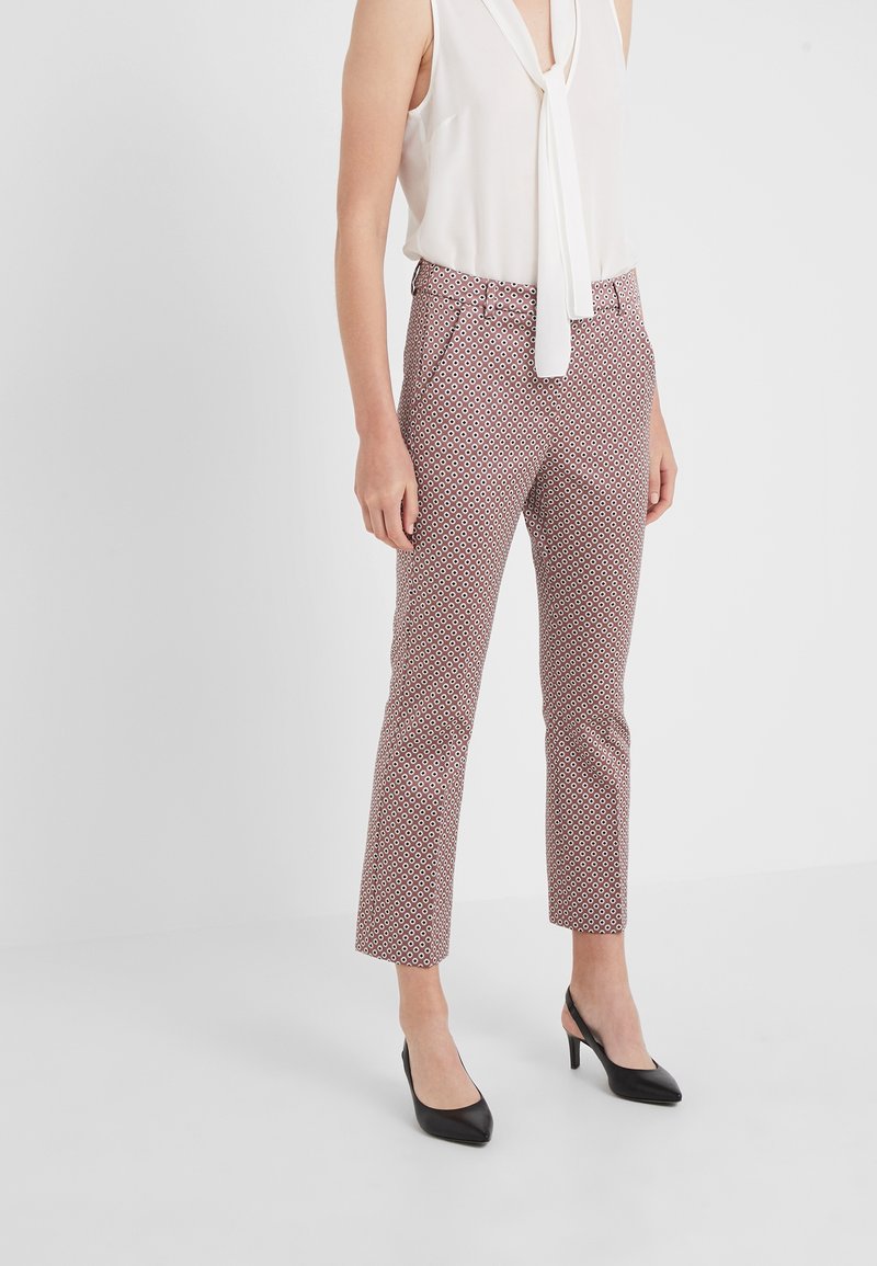 Pantaloni a fantasia in rosso, bianco e blu navy con vestibilità slim, vita media e lunghezza corta, abbinati a tacchi neri e una maglia bianca.