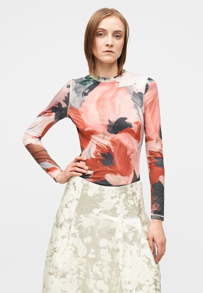 Ilgas rankovėmis viršus su abstrakčiais gėlių raštais rožių, raudonos ir juodos spalvų atspalviuose; derinamas su šviesios metalinės spalvos sijonu.