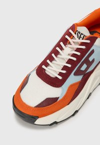 Multicolored sneaker featuring mesh and suede materials. Key colors include orange, maroon, and light blue. Thick rubber sole with laces.
