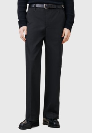 Zwarte pantalon met een recht ontwerp, gemaakt van een gladde stof. Met riem om de taille met een strakke zwarte riem, gecombineerd met gepolijste schoenen.