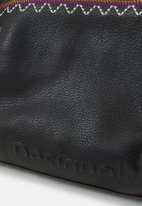 Černý texturovaný kožený povrch s raženým logem "Desigual", zdobený vícebarevnými cik-cak stehy a růžovým a bílým vyšívaným vzorem.