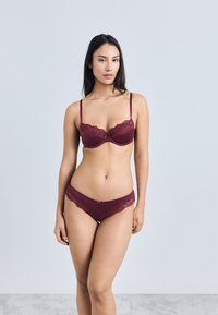 Bordó fehérnemű szett, párnázott melltartóval, csipkedíszítéssel és hozzáillő, csipkebetétes bugyival, amely sima anyagtextúrát mutat.