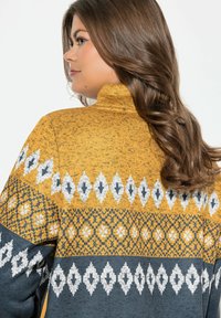 Maglione lavorato a maglia giallo senape con colletto alto. Presenta motivi geometrici bianchi e grigi, colori contrastanti e un tessuto testurizzato.