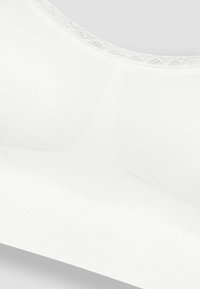 Bralette bianco senza cuciture con una texture a coste e un bordo in pizzo sul décolleté, caratterizzato da un tessuto morbido e un design semplice e funzionale.