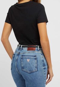 Black short-sleeve t-shirt paired with high-waisted light blue denim jeans featuring a leather label and triangle logo on the back pocket.