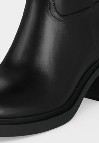Bottine noire en cuir avec bout arrondi et petit talon bloc, finition lisse et couture visible près du panneau latéral élastique.