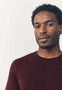 Bordo viigipluus pehmest, siledast kangast, lühikeste varrukatega ja keha järgiva lõikega, ilma nähtavate mustrite või dekoratsioonideta.