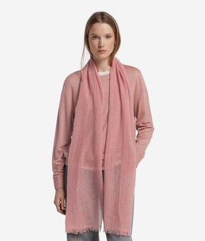 Młoda kobieta ubrana w jasno różowy sweter z długim rękawem i pasujący do niego przejrzysty różowy szalik, stojąca na białym tle.