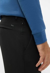 Pantaloni neri con superficie testurizzata, dotati di una tasca laterale con cerniera, abbinati a un felpa blu con polsini a costine.