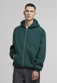 Mørkegrøn zip-up hoodie med foret hætte, frontlommer og ribbede manchetter. Lavet af blødt, tykt stof med en afslappet pasform.