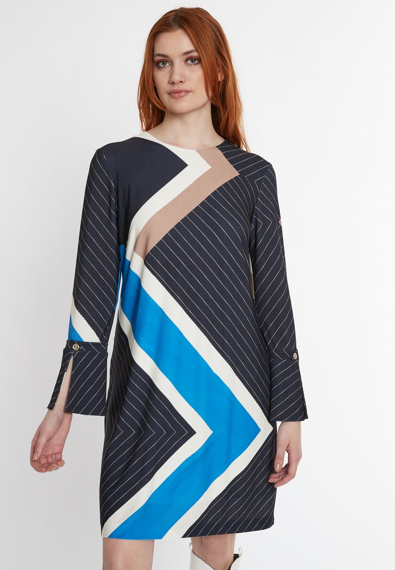Kleid mit geometrischem Muster in Marineblau, Blau, Beige und Weiß. Lange Ärmel mit Schlitzmanschetten und goldenen Akzenten. Glatte Stofftextur.
