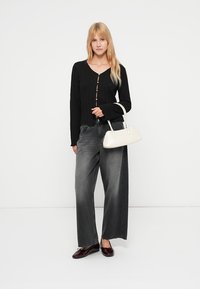 Μαύρη ζακέτα με πλέξη καλώδιο και κούμπωμα με κουμπιά, συνδυασμένη με φαρδιά γκρι τζιν. Αξεσουάρ περιλαμβάνουν μια μικρή λευκή τσάντα και σκουροκόκκινα παπούτσια.