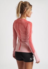 Rød langærmet sportstrøje med struktureret stof og stribede mønstre. Trøjen har et tætsiddende design, der matcher sorte shorts nedenunder.