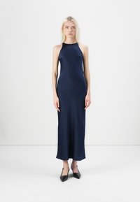 Mørkeblå halterneck maxi kjole med et glat, strømlinet stof. Flade sko med spidse tæer supplerer det minimalistiske design.