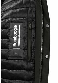 Giacca nera isolata con texture trapuntata, dotata di una tasca con zip e di un logo a patch. L'esterno è di un solido verde scuro.