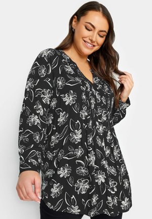 Blusa negra con estampado floral blanco, escote en V y mangas largas con un corte relajado y detalle fruncido en la parte delantera.