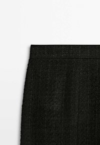 Section de jupe noire texturée taille haute avec détail de ceinture sur fond blanc uni.