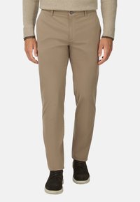 Chinos beige hechos de una tela suave, con un corte recto, cierre de botón y pasadores para cinturón, combinados con zapatos oscuros.