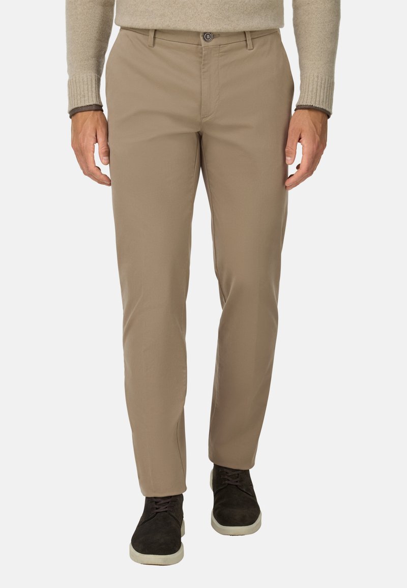 Chinos beige hechos de una tela suave, con un corte recto, cierre de botón y pasadores para cinturón, combinados con zapatos oscuros.