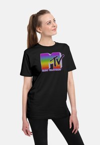Camiseta negra con un logotipo de MTV vibrante y de degradado en púrpura, amarillo y verde, con el texto "MUSIC TELEVISION", ajuste casual y mangas cortas.