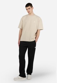 T-shirt beige texturé à manches courtes et pantalon noir au design ajusté, associés à des baskets blanches. Détail de logo simple sur le t-shirt et le pantalon.