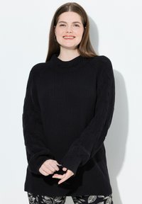 Maglione nero a maglia con collo alto e maniche a treccia testurizzate. Abbinato a pantaloni scuri con motivi a foglia.