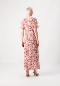 Maxi dress in coral with white floral pattern, short sleeves, and a fit-and-flare silhouette. Worn with strappy heels, viewed from the back.
