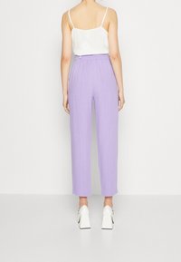 Pantalon palazzo lavande léger à jambes larges, doté d'une ceinture élastique, associé à un haut blanc sans manches et des talons blocs blancs.