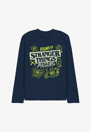 Navy blue long-sleeve shirt with neon green "Stranger Things Tales from 85" text, a bike, radio, flower, skull, and lightning bolt graphics.