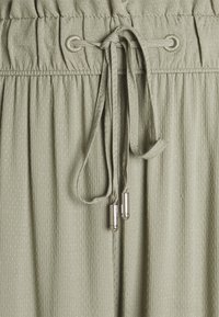 Světlezelená tkanina s texturovaným vzorem, obsahující nařasený pás a šňůrku s kovovými zarážkami.