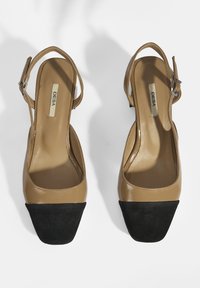 Leather slingback heels with a tan upper and black suede square toe. Features an adjustable strap and smooth interior.