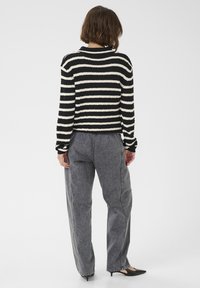 Juodai baltas dryžuotas megztinis su tekstūruotu paviršiumi, trumpu fasonu ir ilgomis rankovėmis, derinamas su laisvais pilkais džinsais.