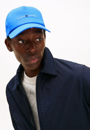Blue baseball cap with "TOMMY HILFIGER" logo, paired with a navy blue jacket and a textured white sweater underneath.