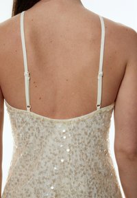 Beadbesetztes Spaghetti-Trägerkleid aus schimmerndem beigen Stoff, mit einem figurbetonten Oberteil und einer zarten, strukturierten Oberfläche aus kleinen Pailletten.