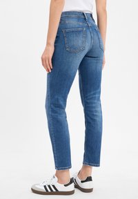 Blaue Jeans aus Denim mit einer taillierten Passform, mittlerer Bundhöhe, Rückentaschen und dezenten Ausbleichungen. Kombiniert mit weißen Sneakers mit schwarzen Akzenten.