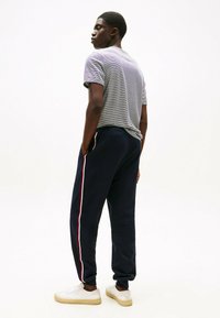 Marineblå sweatpants med røde og hvide striber i siden, parret med en grå stribet t-shirt med korte ærmer og hvide sneakers. Enkelt design, afslappet pasform.