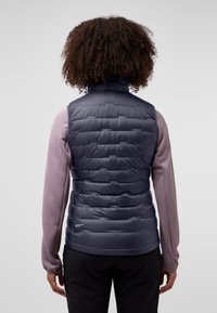 Gilet matelassé bleu marine avec des sections matelassées verticales, un col haut et un design léger. Porté par-dessus une chemise à manches longues texturée lilas clair.