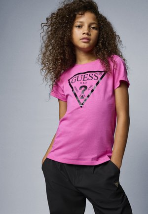 T-shirt en coton rose à manches courtes avec un logo triangulaire noir et du texte, associé à un pantalon baggy noir et à une texture douce.